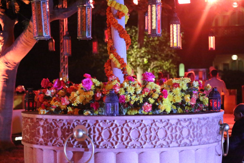 A vibrant floral arrangement with yellow and pink flowers decorates a circular stone structure, adorned with marigold garlands.