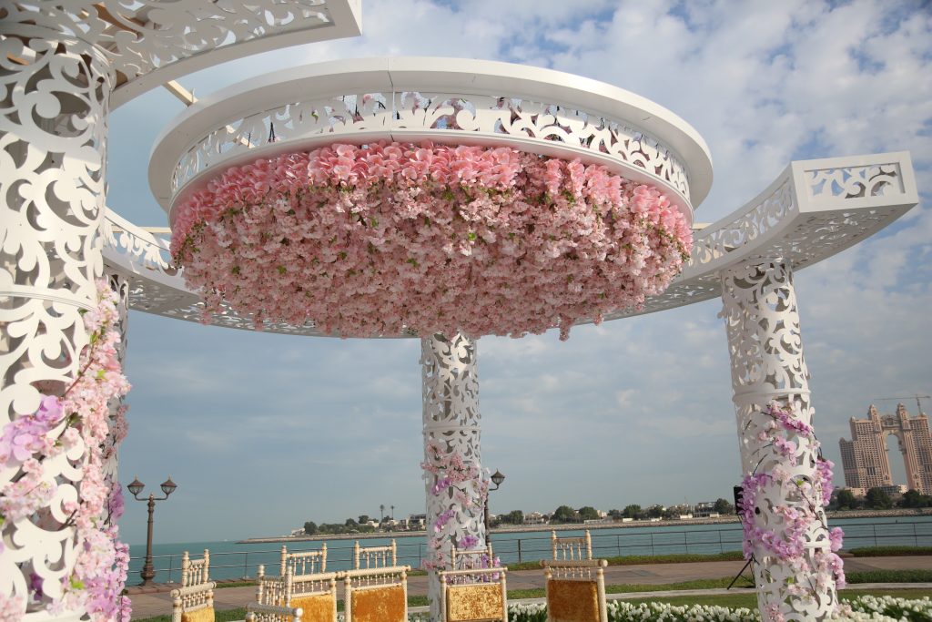 Elegant white floral gazebo adorned with pink flowers, overlooking a serene waterfront.