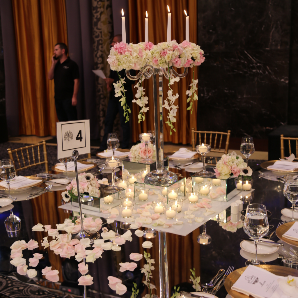 Elegant table setting with a candelabra adorned in pink and white flowers, surrounded by small candles and rose petals, evoking a romantic ambiance.