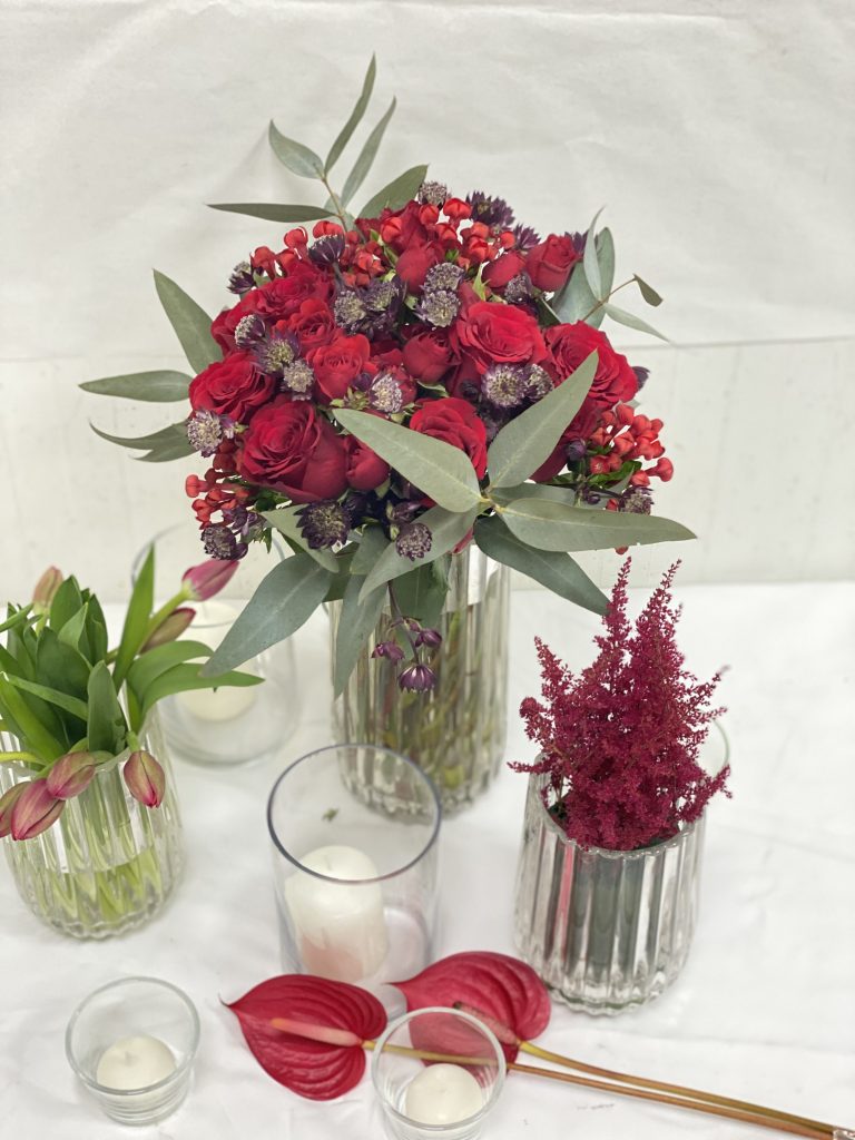 A table adorned with vibrant red flowers and flickering candles, showcasing a decorative arrangement for a floral subscription service.