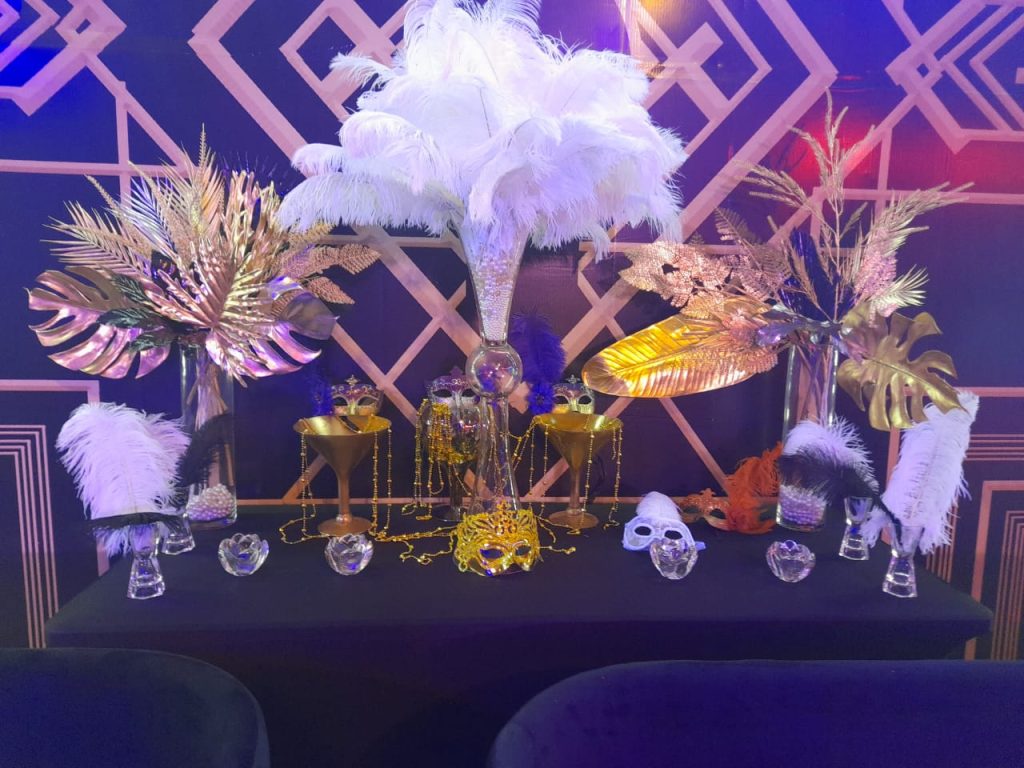 A table adorned with a gold and white tablecloth, decorated with feathers for Halloween flower decor.