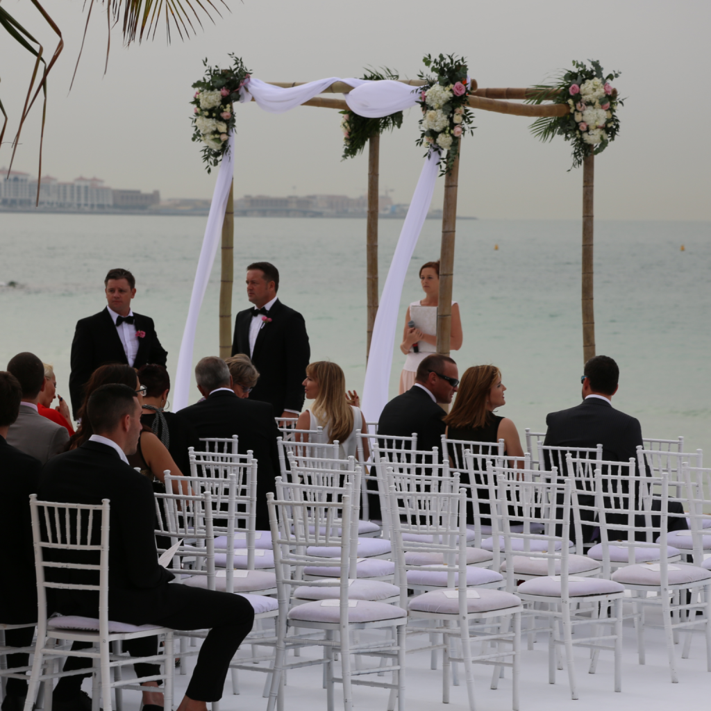 A white wedding arch adorned with flowers, set against a beach backdrop for a Dubai resort wedding.