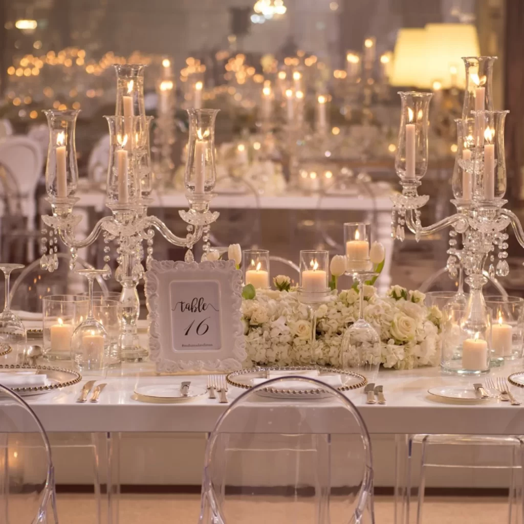 Elegant wedding table setting with crystal candelabras, lit candles, and white floral centerpiece. Glass chairs surround table 16, creating a romantic ambiance.